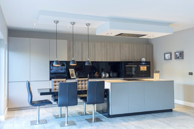 Photo of a medium sized contemporary kitchen/diner in Edinburgh with flat-panel cabinets, grey cabinets, engineered stone countertops, black splashback, glass sheet splashback, black appliances and an island.