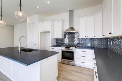 Large classic l-shaped enclosed kitchen in New Orleans with white cabinets, granite worktops, black splashback, metro tiled splashback, stainless steel appliances, light hardwood flooring, an island, a submerged sink, shaker cabinets and brown floors.
