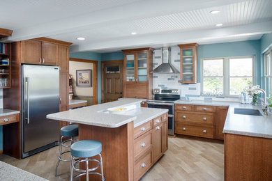 Example of a mid-sized trendy l-shaped light wood floor and beige floor enclosed kitchen design in Other with an undermount sink, shaker cabinets, brown cabinets, solid surface countertops, white backsplash, ceramic backsplash, stainless steel appliances and an island