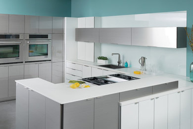 Kitchen - contemporary u-shaped kitchen idea in Chicago with a drop-in sink, flat-panel cabinets, white cabinets, white backsplash, glass sheet backsplash, stainless steel appliances and a peninsula