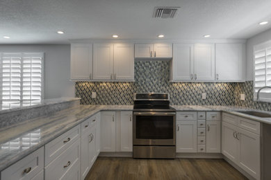 Mid-sized minimalist u-shaped medium tone wood floor eat-in kitchen photo in Tampa with an undermount sink, shaker cabinets, white cabinets, marble countertops, glass tile backsplash, stainless steel appliances and a peninsula