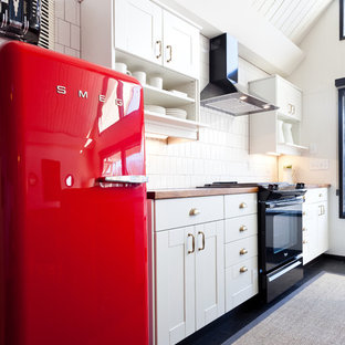 Mid-sized eclectic open concept kitchen pictures - Example of a mid-sized eclectic galley dark wood floor and black floor open concept kitchen design in Portland with white cabinets, wood countertops, black appliances, an island, white backsplash, an undermount sink, shaker cabinets and porcelain backsplash