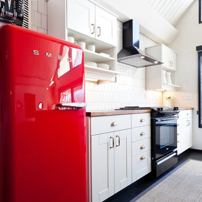 Example of a mid-sized eclectic dark wood floor and black floor kitchen design in Portland with white cabinets, wood countertops, black appliances, an island, white backsplash, an undermount sink, shaker cabinets and porcelain backsplash