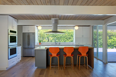 Example of a 1950s light wood floor open concept kitchen design in San Francisco with an undermount sink, shaker cabinets, white cabinets, stainless steel appliances, an island and quartz countertops