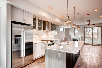 Large urban single-wall medium tone wood floor eat-in kitchen photo in Denver with an undermount sink, recessed-panel cabinets, white cabinets, solid surface countertops, white backsplash, ceramic backsplash, stainless steel appliances and an island