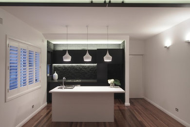 Inredning av ett modernt litet kök, med en undermonterad diskho, släta luckor, svarta skåp, bänkskiva i kvarts, svart stänkskydd, stänkskydd i tegel, rostfria vitvaror, mellanmörkt trägolv och en köksö