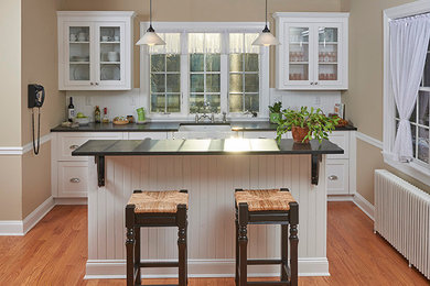 Example of a small farmhouse galley light wood floor eat-in kitchen design in New York with a farmhouse sink, flat-panel cabinets, white cabinets, granite countertops, white backsplash, subway tile backsplash, an island and stainless steel appliances