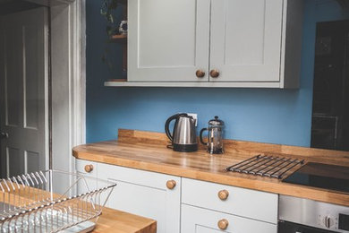 Design ideas for a small traditional l-shaped enclosed kitchen in Devon with a built-in sink, shaker cabinets, grey cabinets, wood worktops, black splashback, glass sheet splashback, integrated appliances, no island and grey floors.