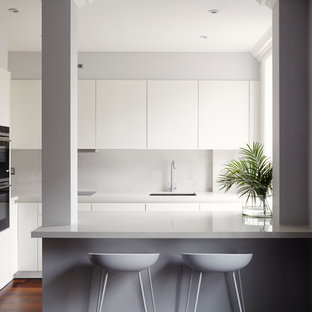 Design ideas for a small contemporary kitchen in London with a submerged sink, flat-panel cabinets, white cabinets, a breakfast bar, brown floors, grey splashback, black appliances and dark hardwood flooring.