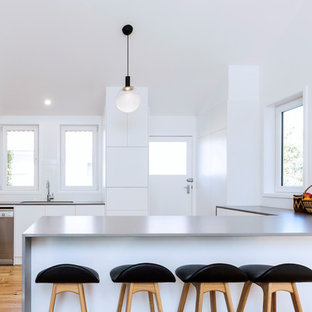 Inspiration for a small contemporary u-shaped open plan kitchen in Canberra - Queanbeyan with an undermount sink, flat-panel cabinets, white cabinets, laminate benchtops, white splashback, porcelain splashback, stainless steel appliances, medium hardwood floors, a peninsula, grey benchtop and brown floor.