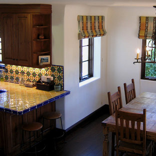Idee per una piccola cucina mediterranea con lavello a doppia vasca, ante con bugna sagomata, ante in legno scuro, top piastrellato, paraspruzzi con piastrelle in ceramica, elettrodomestici in acciaio inossidabile, parquet scuro, penisola, paraspruzzi multicolore, pavimento marrone e top giallo
