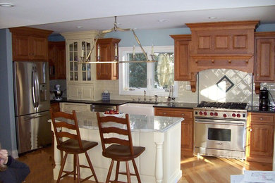 Example of a classic l-shaped eat-in kitchen design in New York with a farmhouse sink, beaded inset cabinets, medium tone wood cabinets, granite countertops, green backsplash, ceramic backsplash and stainless steel appliances