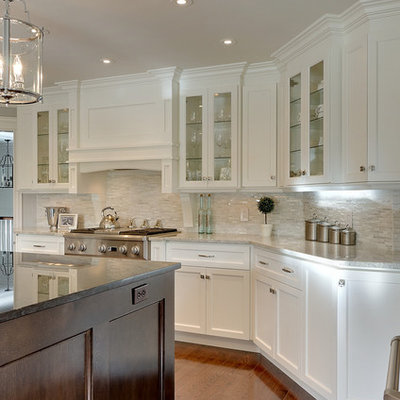 Example of a large transitional l-shaped medium tone wood floor and brown floor kitchen design in Other with white cabinets, stainless steel appliances, shaker cabinets, white backsplash, glass tile backsplash, an island and black countertops