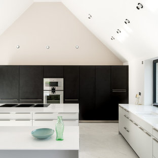 This is an example of a large contemporary l-shaped kitchen in Cheshire with a submerged sink, flat-panel cabinets, composite countertops, integrated appliances, porcelain flooring, multiple islands, white cabinets, window splashback, grey floors and white worktops.