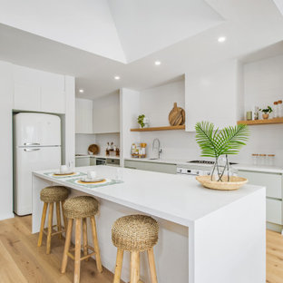 This is an example of a beach style single-wall eat-in kitchen in Melbourne with an undermount sink, white splashback, stainless steel appliances, with island, white benchtop and vaulted.