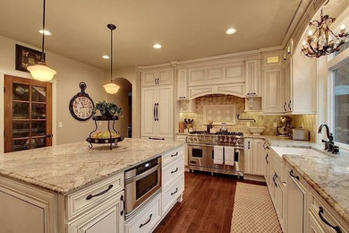 Large elegant l-shaped medium tone wood floor eat-in kitchen photo in Seattle with a farmhouse sink, raised-panel cabinets, distressed cabinets, granite countertops, beige backsplash, ceramic backsplash, stainless steel appliances and an island