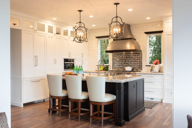 Inspiration for a large transitional l-shaped dark wood floor and brown floor eat-in kitchen remodel in Seattle with a farmhouse sink, white cabinets, granite countertops, metallic backsplash, glass tile backsplash, stainless steel appliances, an island, multicolored countertops and shaker cabinets