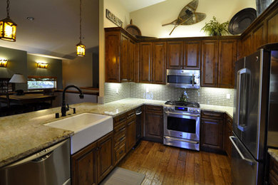 Example of a small mountain style medium tone wood floor kitchen design in Other with a farmhouse sink, raised-panel cabinets, dark wood cabinets, granite countertops, beige backsplash, stainless steel appliances, no island and glass tile backsplash