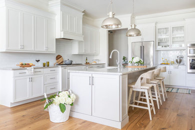 Inspiration for a coastal l-shaped light wood floor and beige floor kitchen remodel in Jacksonville with a farmhouse sink, shaker cabinets, white cabinets, white backsplash, subway tile backsplash, stainless steel appliances, an island and beige countertops