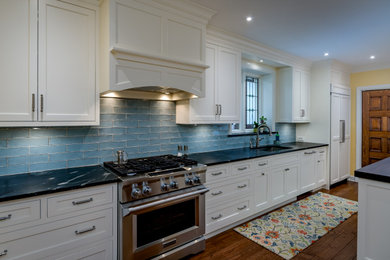Example of a large transitional galley medium tone wood floor eat-in kitchen design in St Louis with an undermount sink, recessed-panel cabinets, white cabinets, soapstone countertops, blue backsplash, subway tile backsplash, stainless steel appliances, an island and black countertops