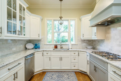 Diseño de cocina tradicional renovada con puertas de armario blancas, encimera de granito, salpicadero blanco, salpicadero de mármol, electrodomésticos de acero inoxidable, suelo de madera clara y una isla