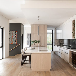 This is an example of a contemporary galley kitchen in Perth with an undermount sink, flat-panel cabinets, white cabinets, black splashback, panelled appliances, medium hardwood floors, with island, brown floor and white benchtop.