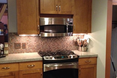 Inspiration for a mid-sized transitional u-shaped ceramic tile enclosed kitchen remodel in Milwaukee with an undermount sink, recessed-panel cabinets, medium tone wood cabinets, quartz countertops, brown backsplash, glass tile backsplash, stainless steel appliances and a peninsula
