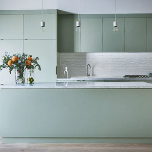 Mid-sized contemporary galley kitchen in Melbourne with a double-bowl sink, flat-panel cabinets, green cabinets, marble benchtops, white splashback, ceramic splashback, light hardwood floors, with island, brown floor, white benchtop and panelled appliances.