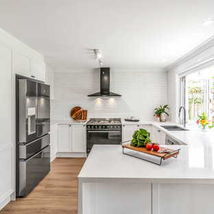 Photo of a mid-sized transitional u-shaped open plan kitchen in Sydney with an undermount sink, shaker cabinets, white cabinets, quartz benchtops, white splashback, subway tile splashback, stainless steel appliances, vinyl floors, a peninsula, brown floor and white benchtop.