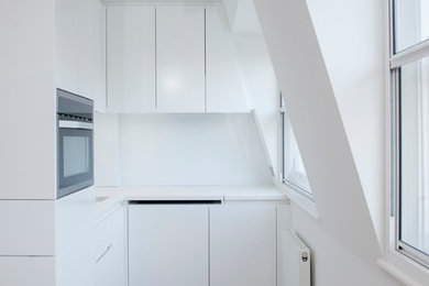 ロンドンにある小さなコンテンポラリースタイルのおしゃれなL型キッチン (一体型シンク、フラットパネル扉のキャビネット、白いキャビネット、人工大理石カウンター、白いキッチンパネル、ガラス板のキッチンパネル、シルバーの調理設備、淡色無垢フローリング) の写真