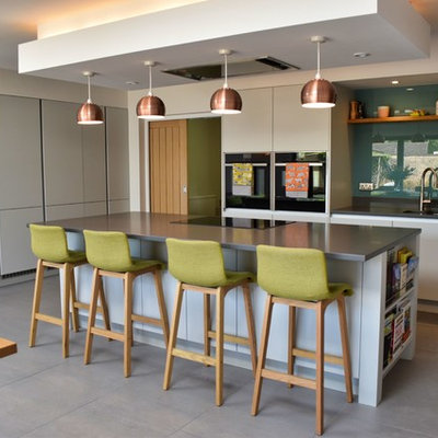 Mid-sized trendy galley ceramic tile and gray floor eat-in kitchen photo in Cambridgeshire with an undermount sink, flat-panel cabinets, gray cabinets, quartzite countertops, black appliances, gray countertops, green backsplash, glass sheet backsplash and an island