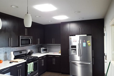 This is an example of a medium sized modern u-shaped kitchen in Los Angeles with a submerged sink, flat-panel cabinets, dark wood cabinets, engineered stone countertops, grey splashback, glass sheet splashback, stainless steel appliances, medium hardwood flooring, a breakfast bar and brown floors.