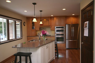 Example of a mid-sized classic single-wall medium tone wood floor and brown floor enclosed kitchen design in Other with a double-bowl sink, raised-panel cabinets, medium tone wood cabinets, granite countertops, stainless steel appliances and an island