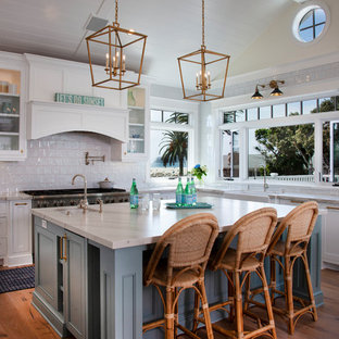 Idee per una cucina costiera di medie dimensioni con lavello stile country, ante in stile shaker, top in quarzo composito, paraspruzzi bianco, paraspruzzi con piastrelle in ceramica, elettrodomestici in acciaio inossidabile, isola, pavimento in legno massello medio, pavimento marrone, top bianco e ante bianche