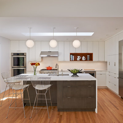 Example of a mid-sized 1960s l-shaped light wood floor and beige floor open concept kitchen design in DC Metro with flat-panel cabinets, white cabinets, an island, quartz countertops, white backsplash, ceramic backsplash, stainless steel appliances and an undermount sink