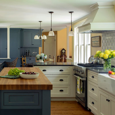 Eat-in kitchen - large country u-shaped medium tone wood floor eat-in kitchen idea in Boston with a farmhouse sink, white backsplash, stainless steel appliances, an island, shaker cabinets, blue cabinets, wood countertops and ceramic backsplash