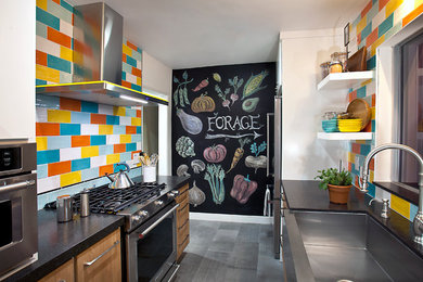 This is an example of a small modern galley enclosed kitchen in Los Angeles with a belfast sink, flat-panel cabinets, distressed cabinets, engineered stone countertops, multi-coloured splashback, ceramic splashback, stainless steel appliances, porcelain flooring, no island, grey floors and black worktops.