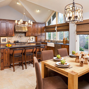Photo of a large country u-shaped eat-in kitchen in New York with a farmhouse sink, raised-panel cabinets, dark wood cabinets, granite benchtops, multi-coloured splashback, slate splashback, stainless steel appliances, travertine floors, with island, beige floor and black benchtop.