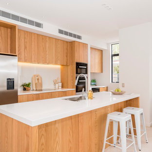 Inspiration for a mid-sized contemporary galley kitchen in Christchurch with an undermount sink, flat-panel cabinets, light wood cabinets, quartz benchtops, white splashback, glass sheet splashback, stainless steel appliances, porcelain floors, with island, beige floor and white benchtop.