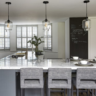 Design ideas for a large contemporary galley open plan kitchen in London with an integrated sink, recessed-panel cabinets, grey cabinets, marble benchtops, metallic splashback, mirror splashback, stainless steel appliances, dark hardwood floors, a peninsula, brown floor and white benchtop.