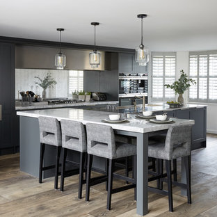Large contemporary galley open plan kitchen in London with an integrated sink, recessed-panel cabinets, grey cabinets, marble benchtops, metallic splashback, mirror splashback, stainless steel appliances, dark hardwood floors, a peninsula, brown floor and white benchtop.