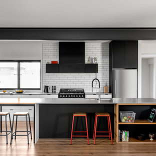 This is an example of a contemporary kitchen in Other with an undermount sink, flat-panel cabinets, white cabinets, white splashback, subway tile splashback, stainless steel appliances, medium hardwood floors, with island and grey benchtop.
