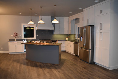 Photo of a large traditional l-shaped kitchen/diner in Seattle with a submerged sink, shaker cabinets, white cabinets, engineered stone countertops, blue splashback, glass tiled splashback, stainless steel appliances, laminate floors, an island and grey floors.