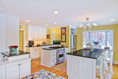 Example of a mid-sized classic u-shaped light wood floor eat-in kitchen design in Detroit with an undermount sink, recessed-panel cabinets, white cabinets, solid surface countertops, white backsplash, ceramic backsplash, stainless steel appliances and two islands
