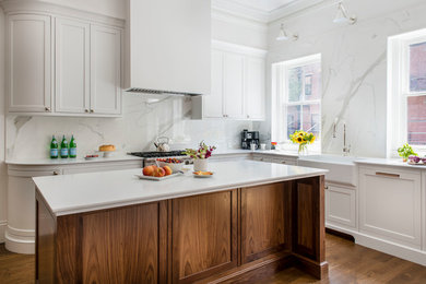 Large classic l-shaped kitchen/diner in Boston with a belfast sink, beaded cabinets, white cabinets, engineered stone countertops, white splashback, integrated appliances, an island and white worktops.