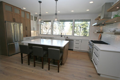 Design ideas for a medium sized traditional u-shaped open plan kitchen in Seattle with a belfast sink, shaker cabinets, white cabinets, engineered stone countertops, white splashback, porcelain splashback, stainless steel appliances, light hardwood flooring, an island, grey floors and white worktops.