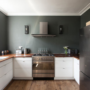 This is an example of a contemporary u-shaped kitchen in London with a double-bowl sink, flat-panel cabinets, white cabinets, wood worktops, stainless steel appliances, medium hardwood flooring, brown floors and brown worktops.