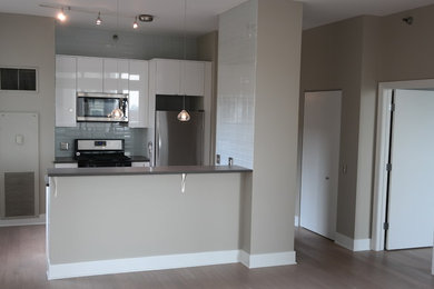 Example of a mid-sized minimalist kitchen design in Chicago with a drop-in sink, flat-panel cabinets, white cabinets, blue backsplash, glass tile backsplash, stainless steel appliances and an island