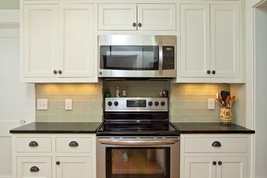 ミネアポリスにある高級な小さなトラディショナルスタイルのおしゃれな独立型キッチン (アンダーカウンターシンク、落し込みパネル扉のキャビネット、白いキャビネット、ソープストーンカウンター、緑のキッチンパネル、ガラスタイルのキッチンパネル、シルバーの調理設備、淡色無垢フローリング、アイランドなし、ベージュの床) の写真