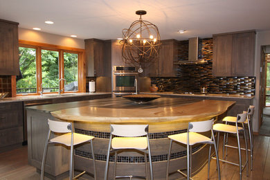 Modern inredning av ett stort kök, med en undermonterad diskho, skåp i shakerstil, grå skåp, granitbänkskiva, stänkskydd med metallisk yta, stänkskydd i glaskakel, rostfria vitvaror, mellanmörkt trägolv, en köksö och brunt golv